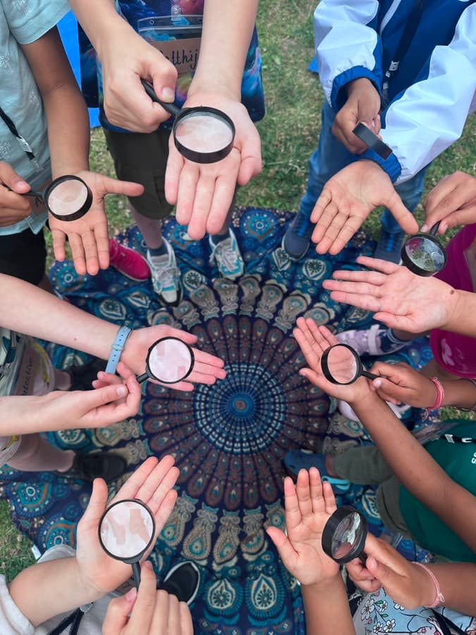Children examining the mandala mat with magnifying glasses