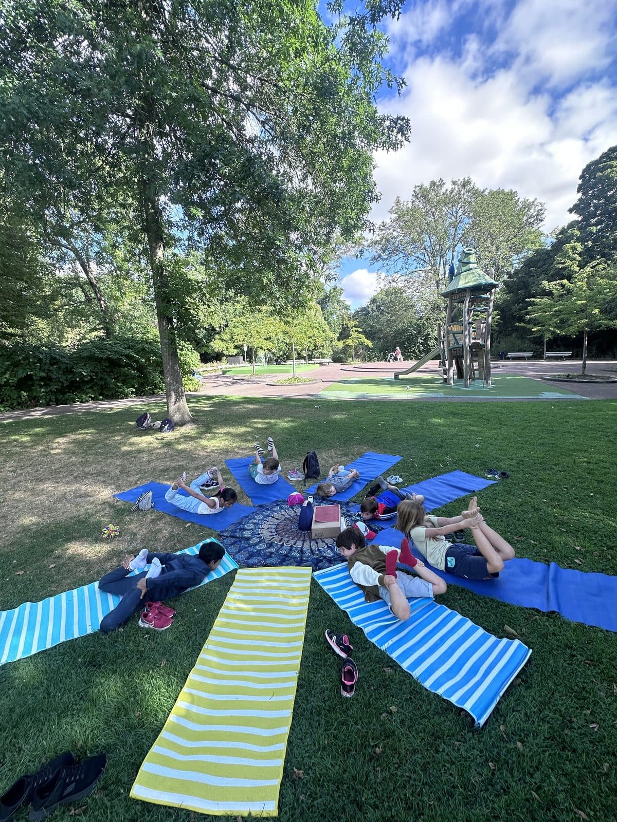 Children lying in a circle on mats in the park